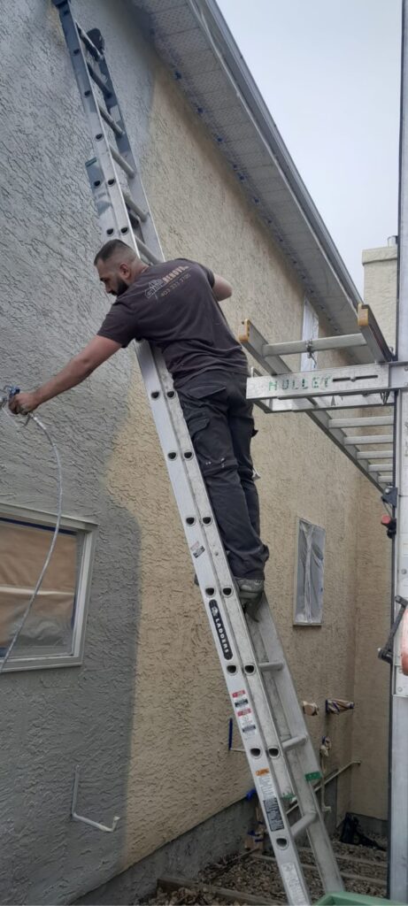 Spraying primer and paint on stucco in Calgary by Renovo Painting Inc